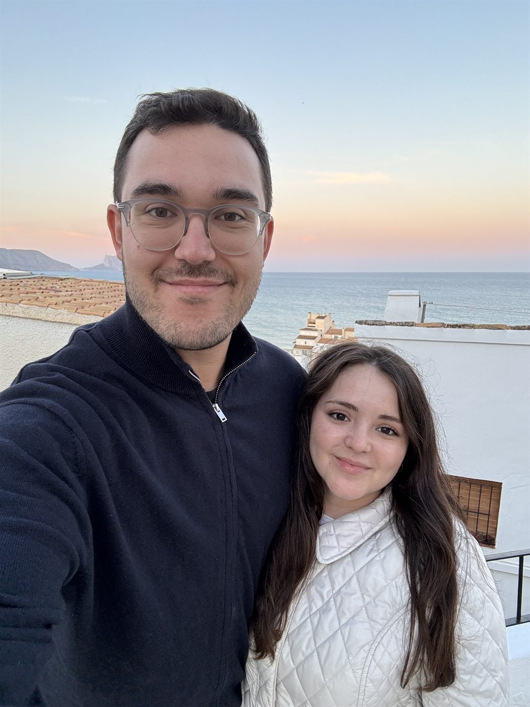 Los dos en una terraza con el mar y el cielo rosado del atardecer al fondo