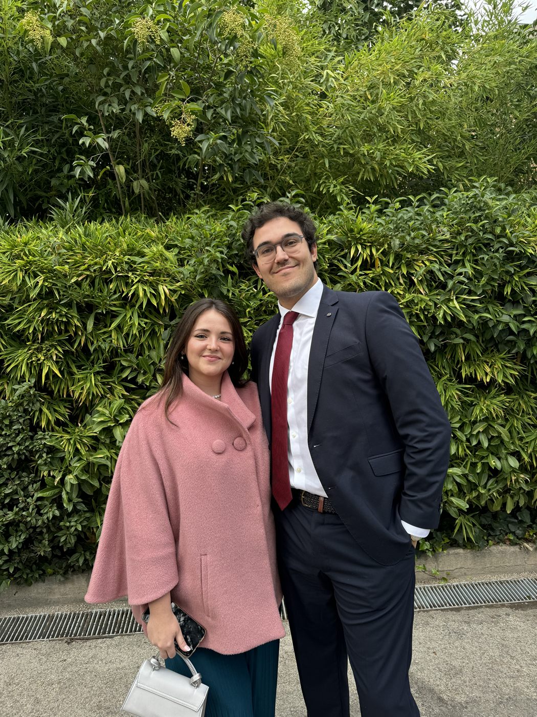 Los dos arreglados en un jardín, ella con abrigo rosa y él de traje