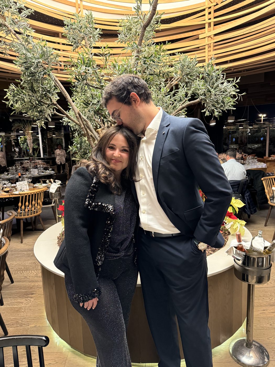 Los dos abrazados de noche en un local con olivos, vestidos de fiesta