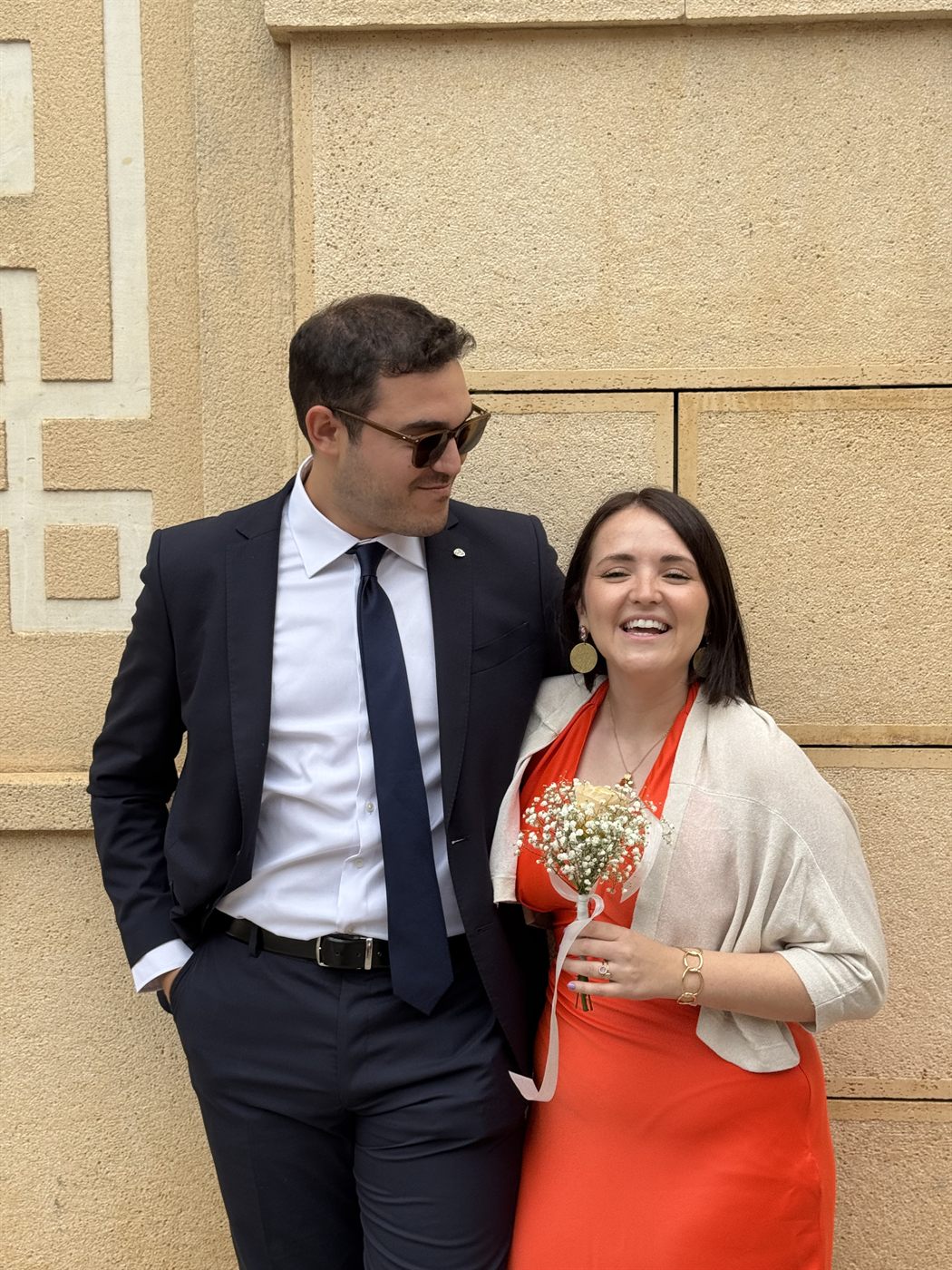 Los dos apoyados en una pared de piedra, ella con vestido rojo y un ramito en la mano